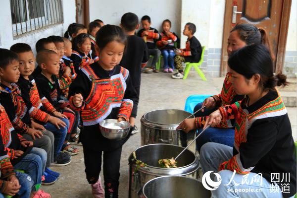 美姑县洛俄依甘乡新农村幼教点的孩子们排队打饭。人民网 朱虹 摄